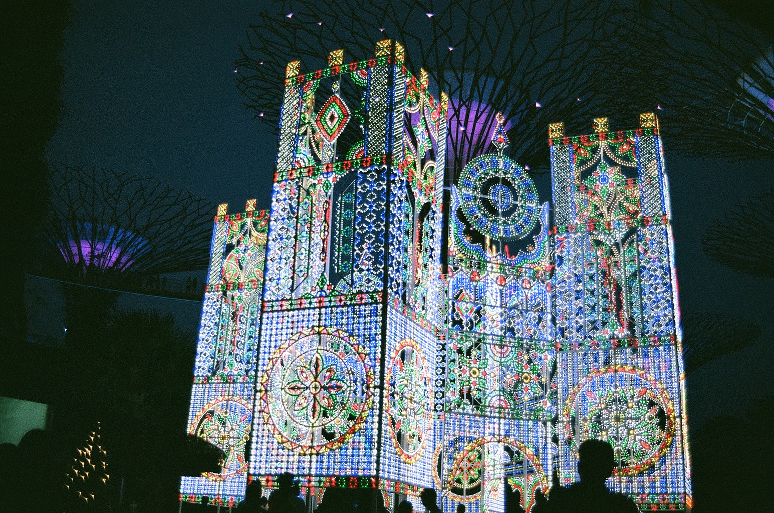 Photo of a light installation at dusk, it is large and consists of geometric shapes decorating panels that are put together into a big structure