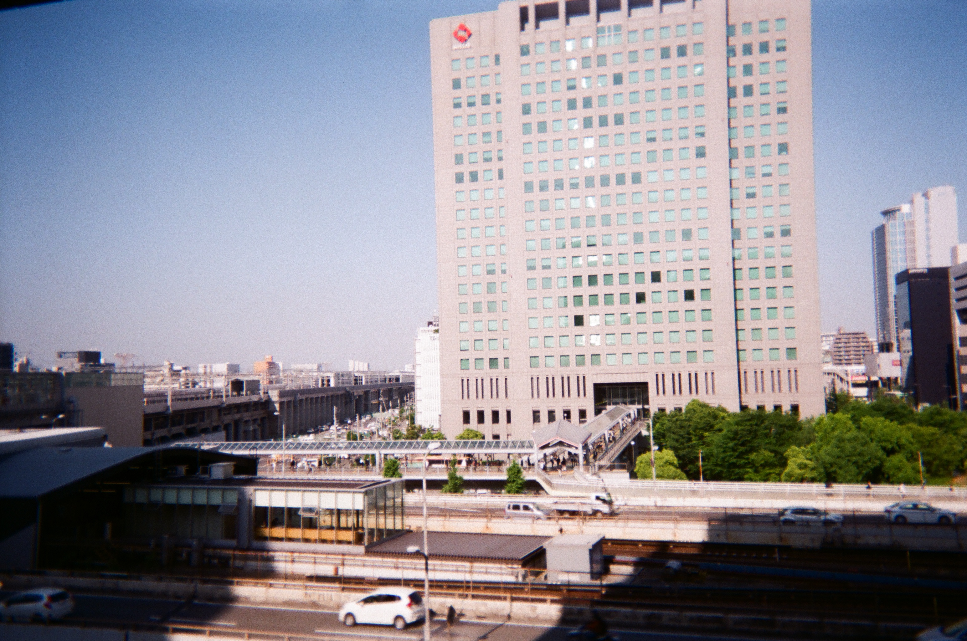 Photo from above ground level of roads and the buildings opposite the roads. Time of day is morning and the sky is clear