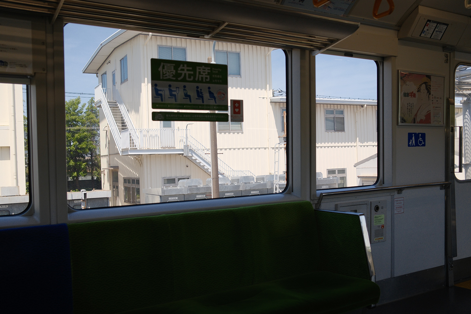 Photo of the interior of a train. A white building in creamy tones can be seen through the window. It's sunny and the sky is a pale milky blue.