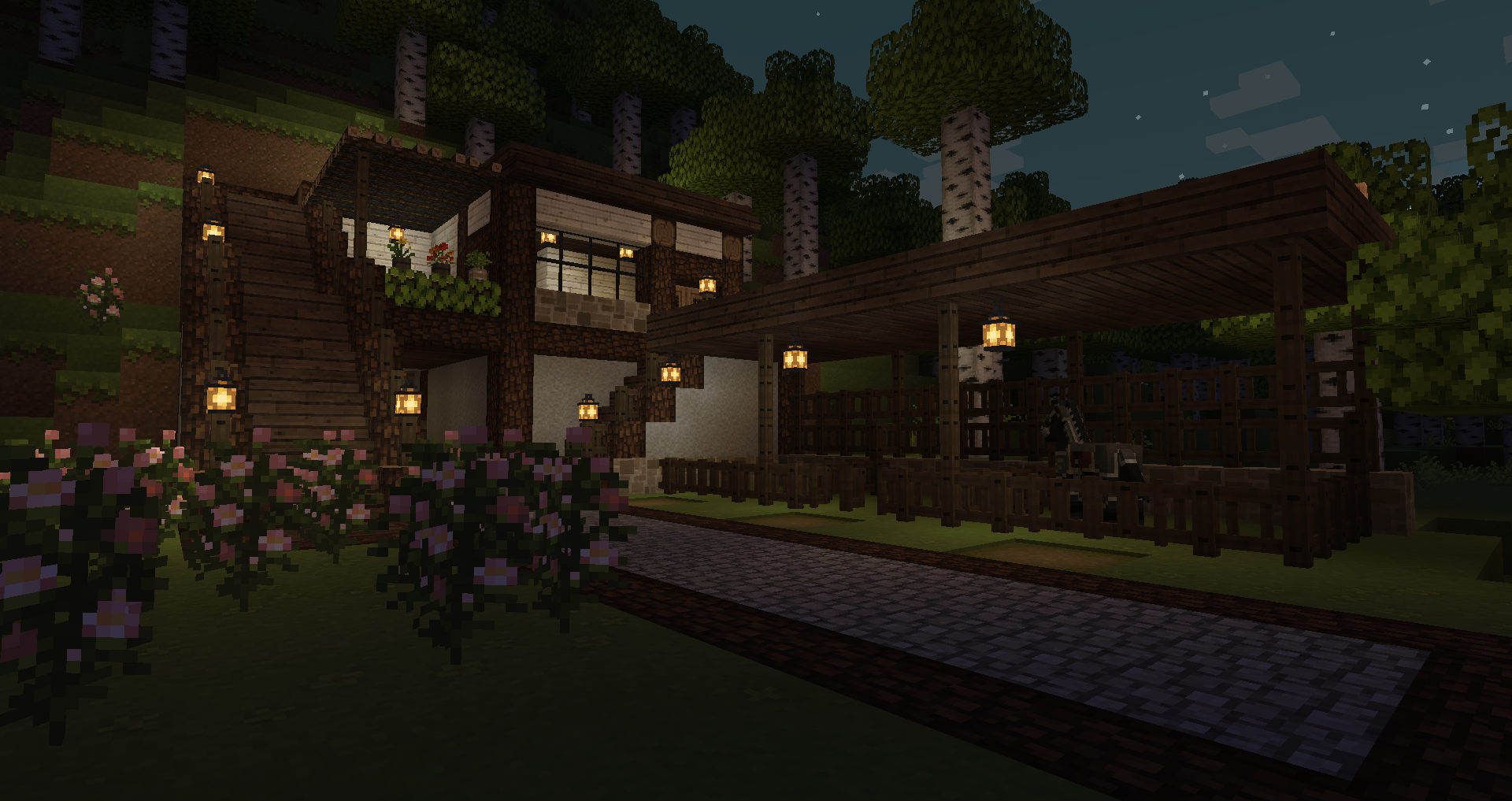 Screenshot of a cozy wood and stone building in Minecraft, built into the side of a hill above and around the entrance to a tunnel. There is a stable with a single horse in it in front of the building. Natural flowers and birch trees surround the scene.