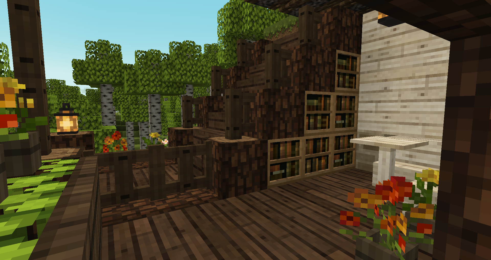 Screenshot of a small porch in Minecraft. There is a little sheltered area closed off by some fence gates, and a staircase going up outside the fence gates. Built into the side of the staircase is some bookshelves, and near them, a corner bench and a table in white birch wood. The floor is also wood. Some flowerpots with flowers in them have been placed around for decoration, and lanterns are used for lighting.